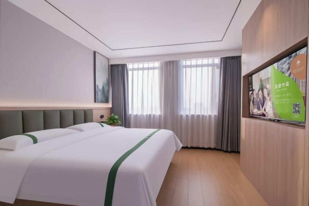 A hotel room with a large bed, a television, a window with curtains, and a poster on the wall.