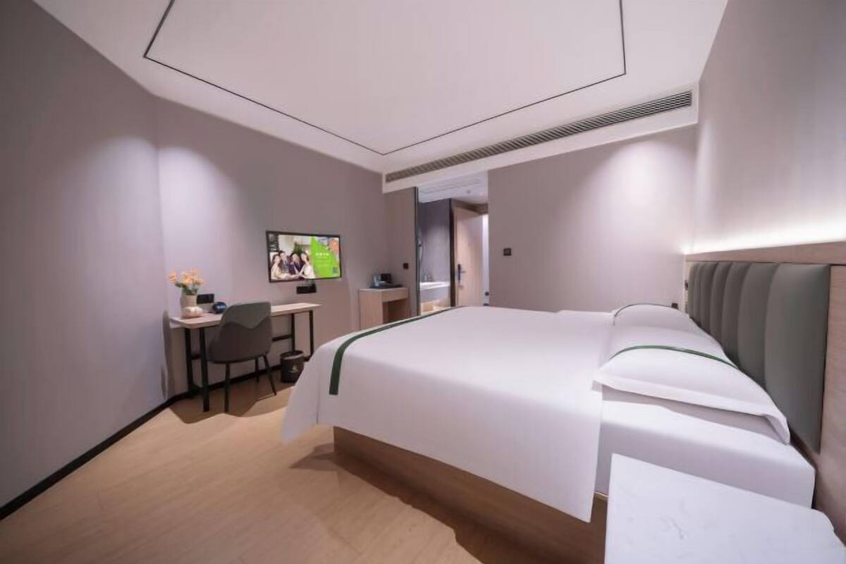 Ein modernes Hotelzimmer mit einem großen Bett, einem Schreibtisch mit Stuhl, einem Fernseher und einem durch eine offene Tür einsehbaren Badezimmer.