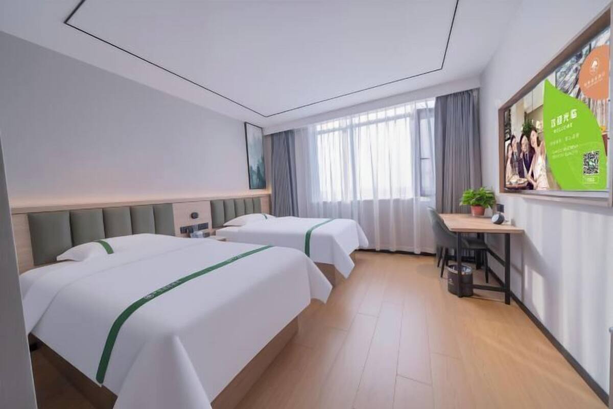 Ein Hotelzimmer mit zwei Betten, einem Schreibtisch, einem Stuhl, einem Fenster mit Vorhängen und einem Bild an der Wand.