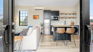A modern kitchen with a refrigerator, microwave, and sink, a dining area with two chairs, and a sofa. - Rooftop Retreat (Ottawa)