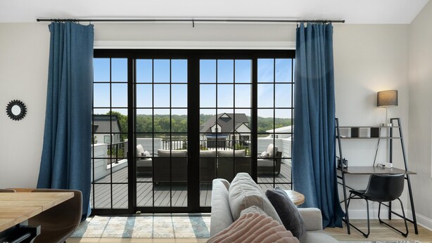 A modern living room with a large sliding glass door leading to a balcony, a dining area, and a workspace with a desk and chair. - Rooftop Retreat (Ottawa)