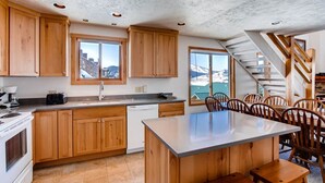 A kitchen with wooden cabinets, a central island, and a view of a snowy landscape through large windows. - Rustic Mountain Retreat with Stunning Views (Crested Butte)