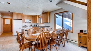 A modern kitchen with wooden cabinets, a central island, and a dining area with wooden chairs. - Rustic Mountain Retreat with Stunning Views (Crested Butte)