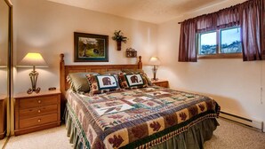 A bedroom with a large bed, two bedside tables, a nightstand, a window with curtains, a framed picture on the wall, and a small plant. - Rustic Mountain Retreat with Stunning Views (Crested Butte)