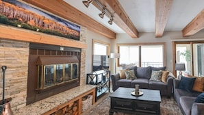 A cozy living room with a fireplace, a sofa set, and a large window offering a view. - Spacious 2BR Condo | Stunning Mountain Views (Crested Butte)