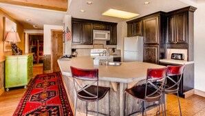A kitchen with dark wooden cabinets, a white microwave, and a large island with bar stools. - Spacious 2BR Condo | Stunning Mountain Views (Crested Butte)