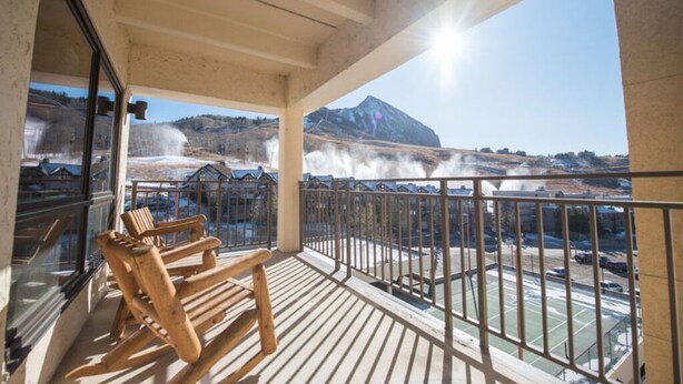 A balcony with wooden chairs, a view of a mountain, and a hot spring. - Spacious 2BR Condo | Stunning Mountain Views (Crested Butte)