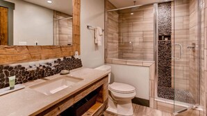 A modern bathroom with a stone mosaic backsplash, a wooden vanity, a large mirror, and a glass-enclosed shower area. - Modern 3BR Condo | Stunning Mountain Views (Crested Butte)