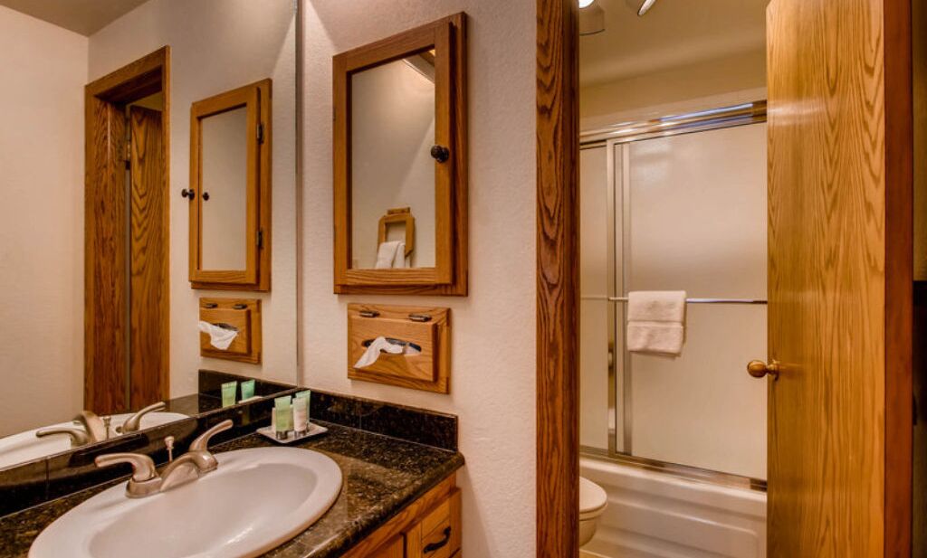 A bathroom with two sinks, wooden cabinets, a mirror, and a glass-enclosed shower.