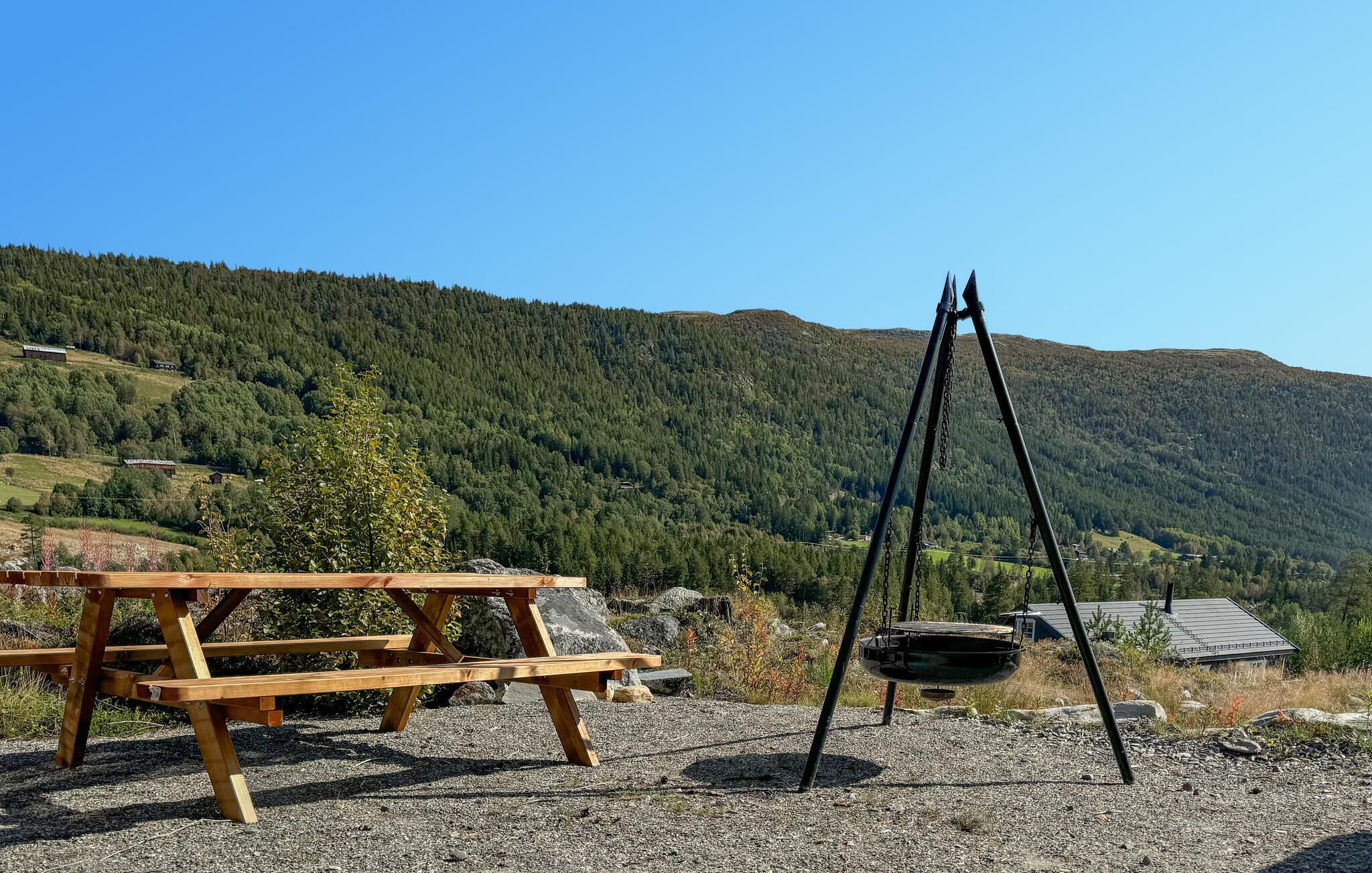 A wooden picnic table and a swing set in a natural setting with a mountainous backdrop.