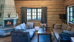 Interior de una cabaña de troncos con chimenea, dos sofás, una mesa de centro y un televisor.