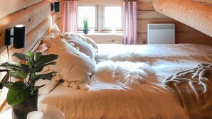 Un dormitorio acogedor con una cama grande, una mesita de noche con una planta, una lámpara y una ventana con cortinas.