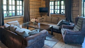 Interior de una cabaña de troncos con sofá, sillón y mesa de centro.