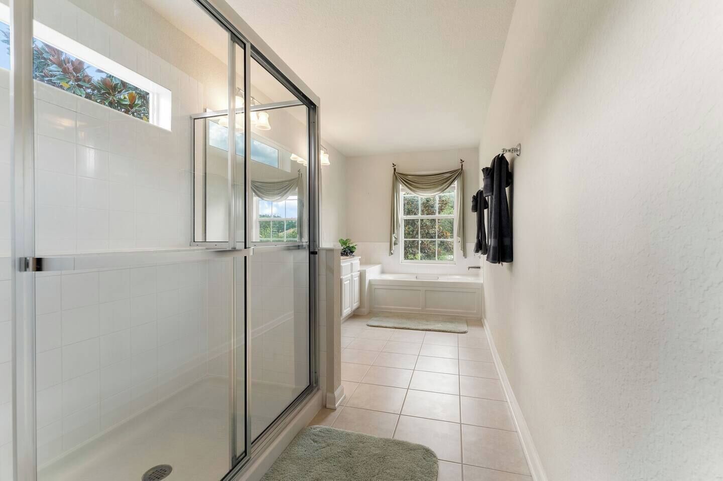 A bathroom with a glass shower door, a bathtub, and a window with curtains.