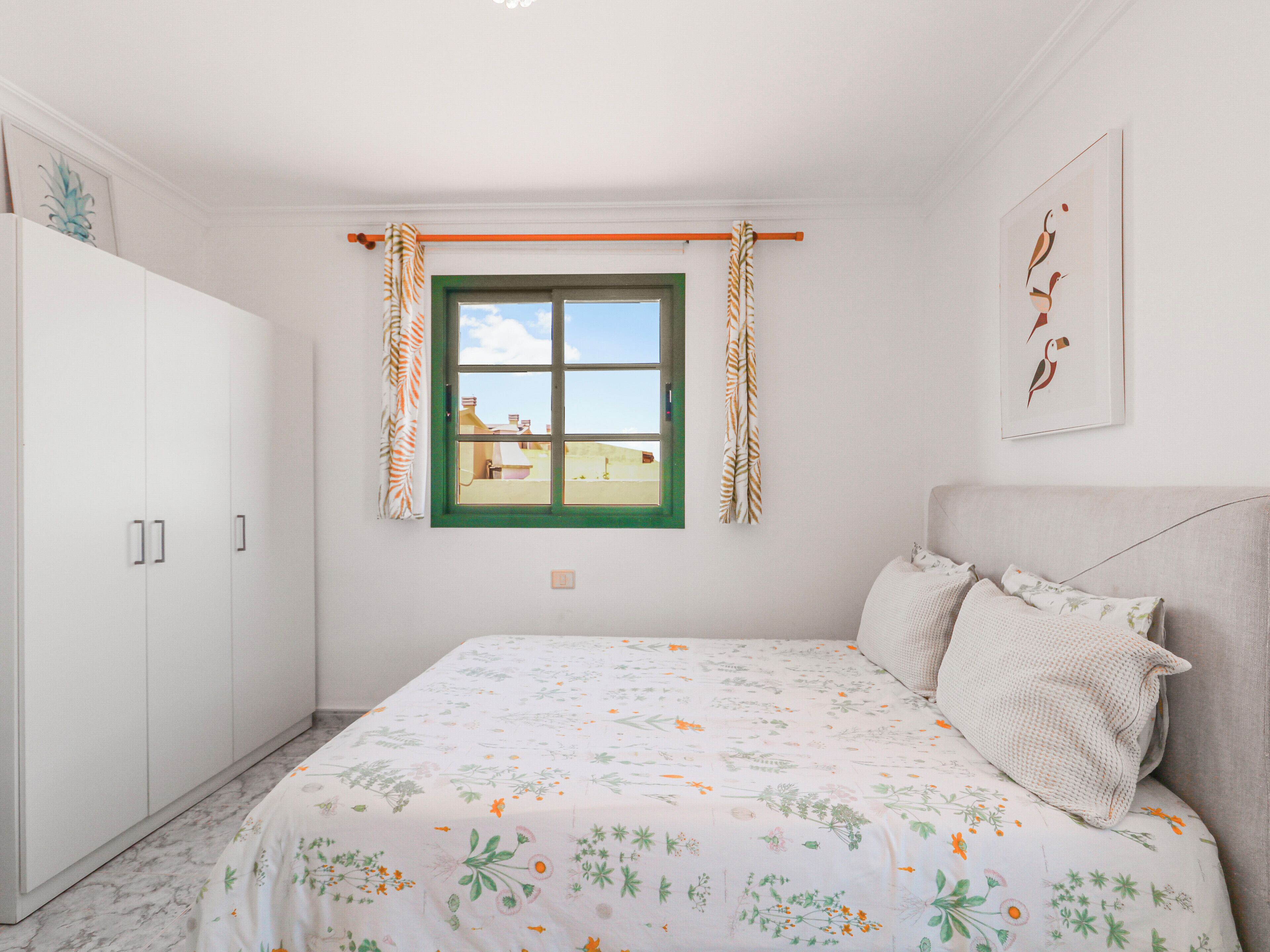 A bedroom with a bed, a wardrobe, a window with curtains, and a wall-mounted picture.