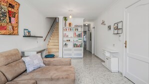 Un saló modern amb un sofà beix, una biblioteca, una escala i un passadís que condueix a una altra habitació.