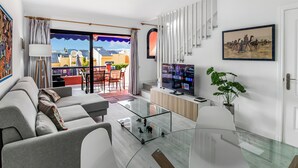 Una sala de estar moderna con un conjunto de sofá, una mesa de centro de vidrio, un televisor y un balcón con vistas.