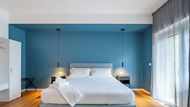 Ein modernes Schlafzimmer mit einem großen Bett, zwei Nachttischen, einem Kleiderschrank und einem Fenster mit Vorhängen.
