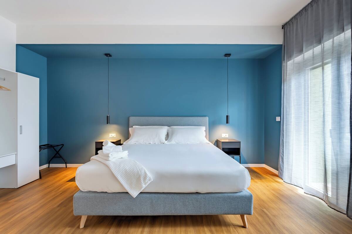 A modern bedroom with a large bed, two bedside tables, a wardrobe, and a window with curtains.