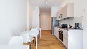 Eine moderne Küche mit weißen Schränken, einem Einbauofen und einer Mikrowelle. Es gibt eine Essecke mit weißen Stühlen und einem Tisch.