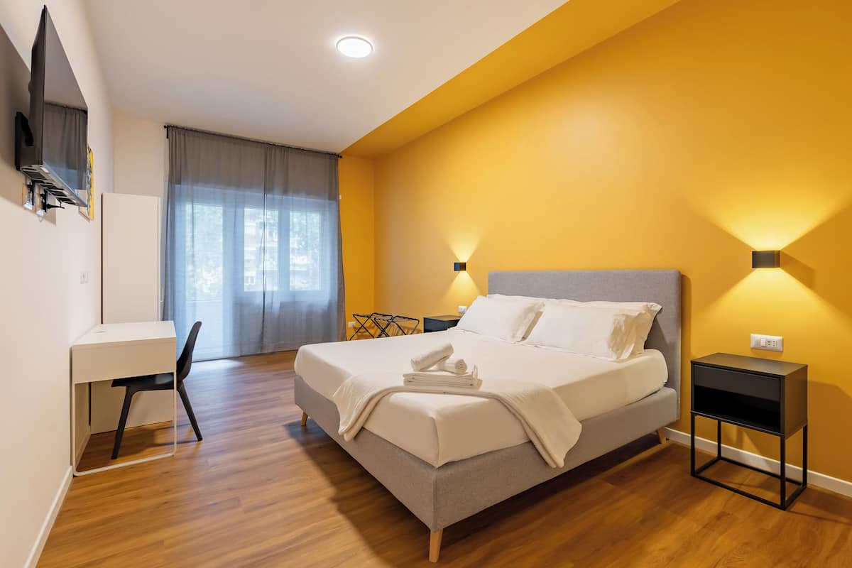 A modern hotel room with a bed, a desk, and a chair.