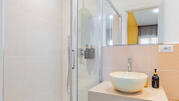 A modern bathroom with a glass shower enclosure, a white sink, and a wooden vanity.