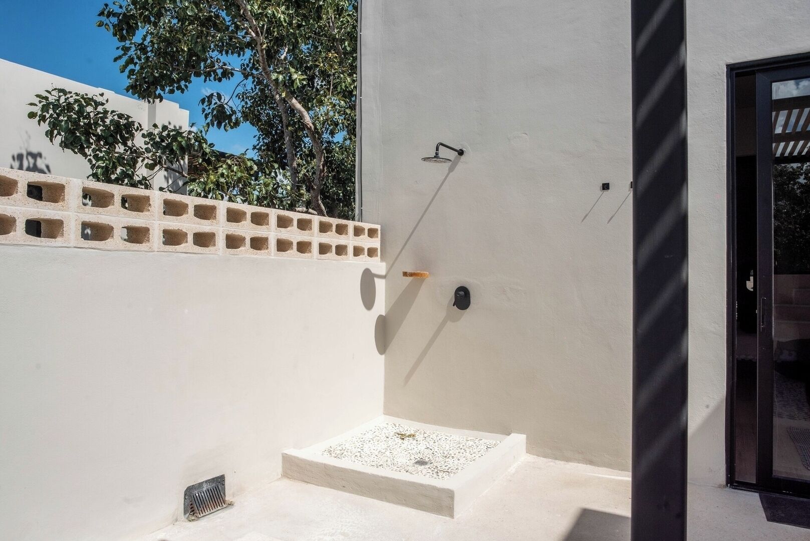 A modern outdoor shower area with a concrete floor, a small step leading up to it, and a wall with a brick pattern.
