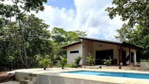 A modern house with a swimming pool, surrounded by trees and a gravel area.