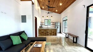 A modern living room with a black sofa, green cushions, a wooden coffee table, and a kitchen in the background.