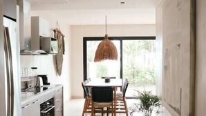 Et moderne køkken med spiseplads, en hængende lampe og et stort vindue der lukker naturligt lys ind.