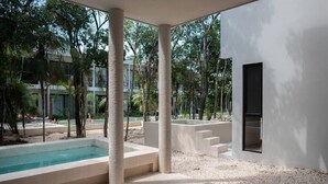 A modern outdoor pool area with steps leading to a pool, surrounded by palm trees and a white building with a window. - Luxury House in the Jungle with Pool by BT Homes (Tulum)