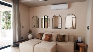 A modern living room with a sectional sofa, three wall-mounted mirrors, and a small side table. - Luxury House in the Jungle with Pool by BT Homes (Tulum)