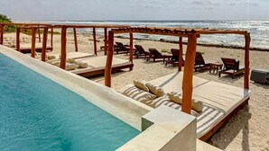 Et poolområde med liggestole og en pergola med udsigt over stranden.