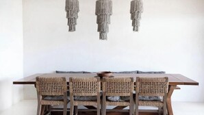 A dining table with four chairs, each with a woven seat and backrest, and three hanging pendant lights above. - Luxury and Serenity by the Sea by BT Homes (Tulum)