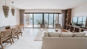 A modern living room with a large TV, wooden dining table, and a sofa. - Luxury and Serenity by the Sea by BT Homes (Tulum)
