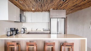 A modern kitchen with a central island, stainless steel appliances, and wooden bar stools. - Luxury and Serenity by the Sea by BT Homes (Tulum)