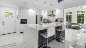 A modern kitchen with a marble island, bar stools, and a built-in oven.