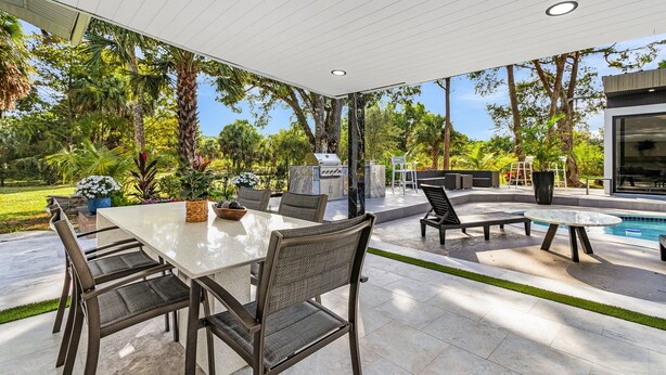 An outdoor patio with a dining table and chairs, a pool, and a barbecue area.