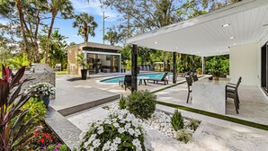A modern outdoor patio with a pool, seating area, and lush greenery.