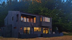 A modern two-story wooden house with large windows and a flat roof, surrounded by trees. -  NEW 3BR/3Bath Ocean Views 2-min walk to Bluff Trail Close to Town (Sea Ranch)