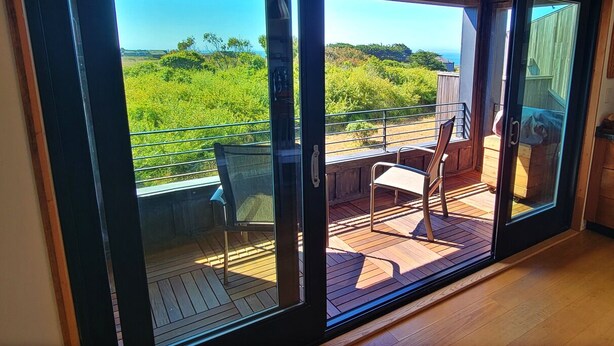 A sliding glass door leading to an outdoor deck with a view of greenery and hills. -  NEW 3BR/3Bath Ocean Views 2-min walk to Bluff Trail Close to Town (Sea Ranch)