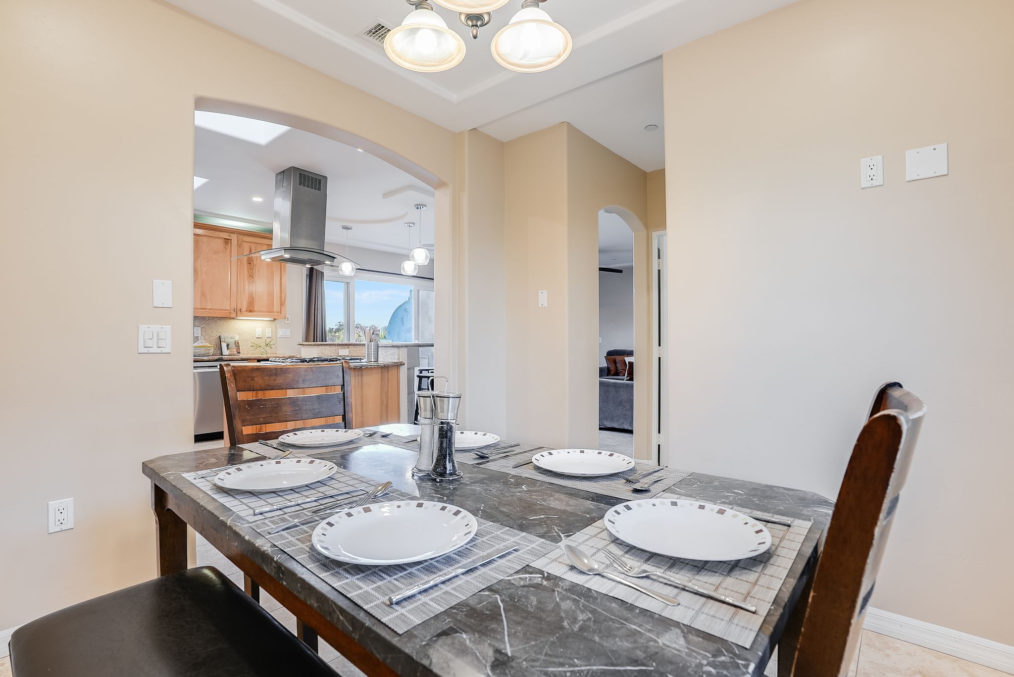A dining area with a marble table set for four, wooden chairs, and a view into the kitchen.