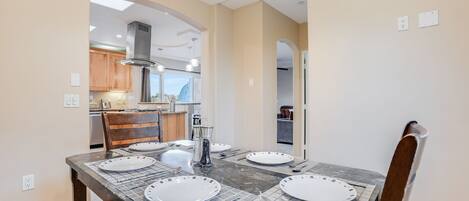 A dining area with a marble table set for four, wooden chairs, and a view into the kitchen.