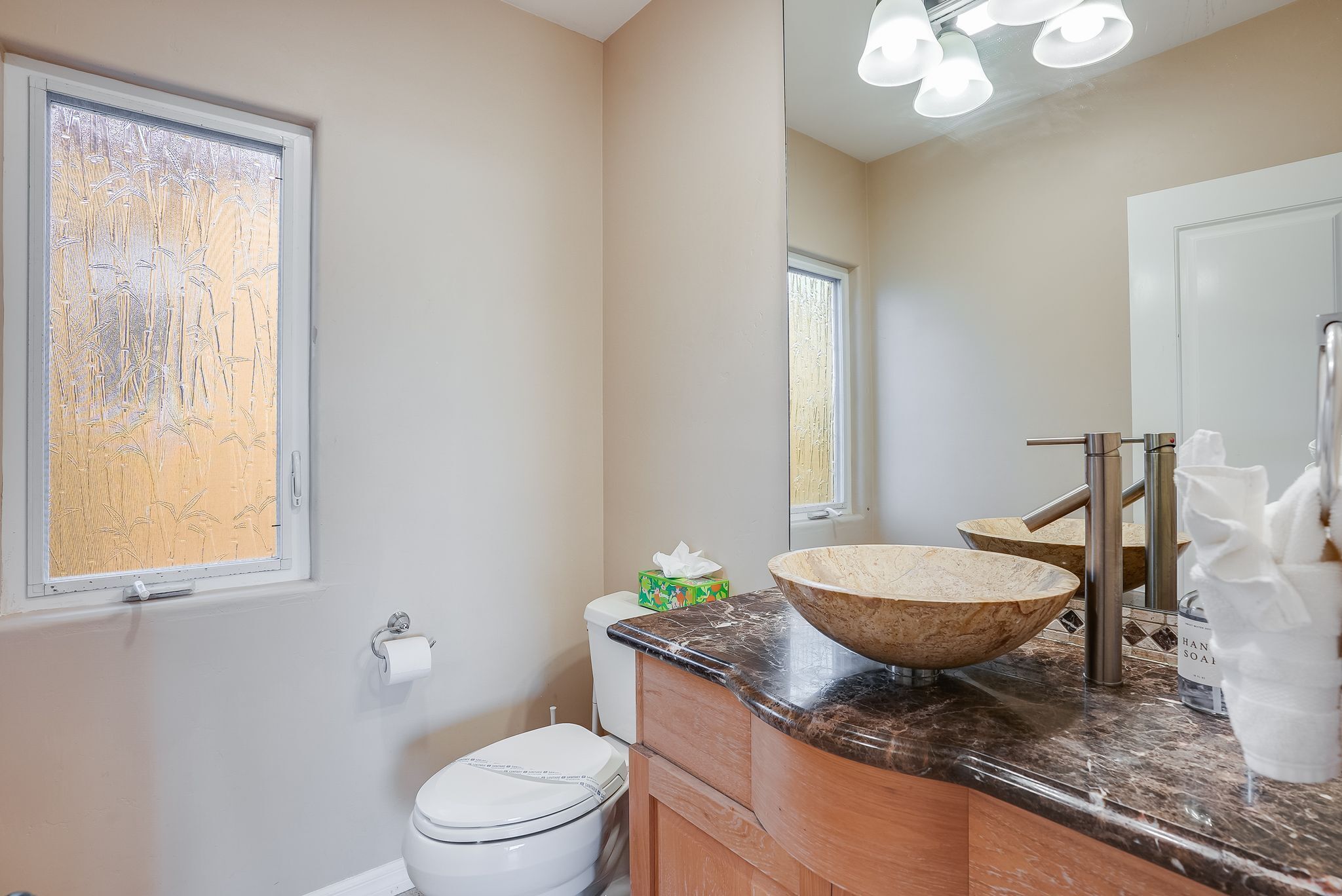 Een badkamer met een groot raam, een toilet, een wastafel met een brede kom en een spiegel.