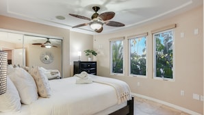 A bedroom with a large bed, a ceiling fan, a dresser, and a window with a view of greenery. - Beach Dream - Steps to the boardwalk & beach with AC, WiFi, deck, prime location! (San Diego)