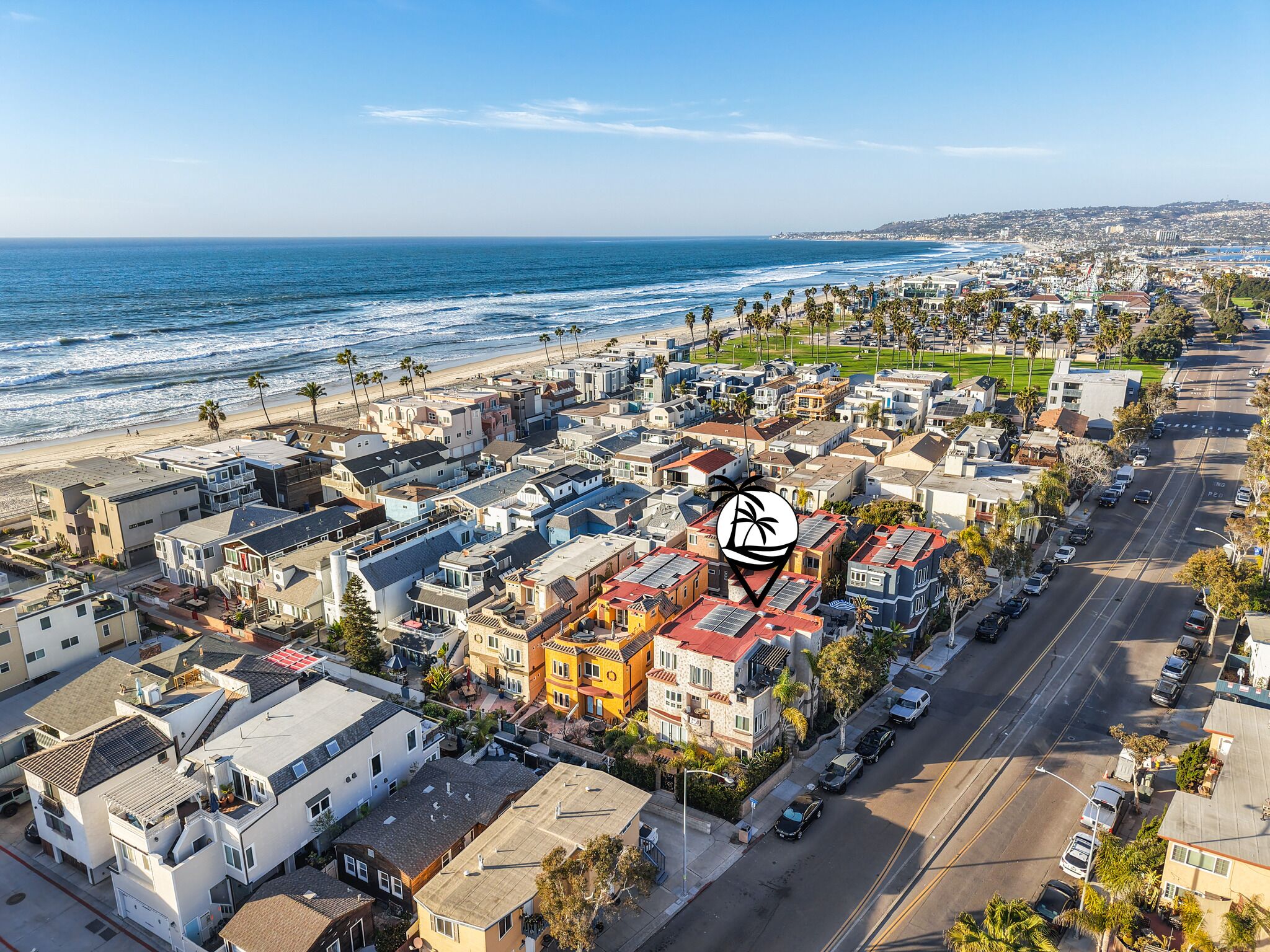 An aerial view of a coastal residential area with houses, a beach, and a clear sky.