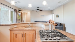 A kitchen with a granite countertop, wooden cabinets, a gas stove, and pendant lighting. - Beach Dream - Steps to the boardwalk & beach with AC, WiFi, deck, prime location! (San Diego)