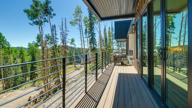 En træterrasse med gelænder i metal, der kigger ud over et skovområde.