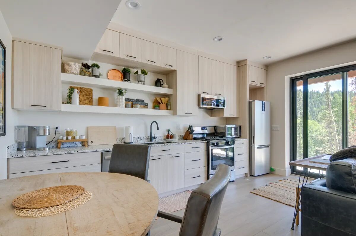 A modern kitchen with light wood cabinets, a central island, and a dining area with a round table.