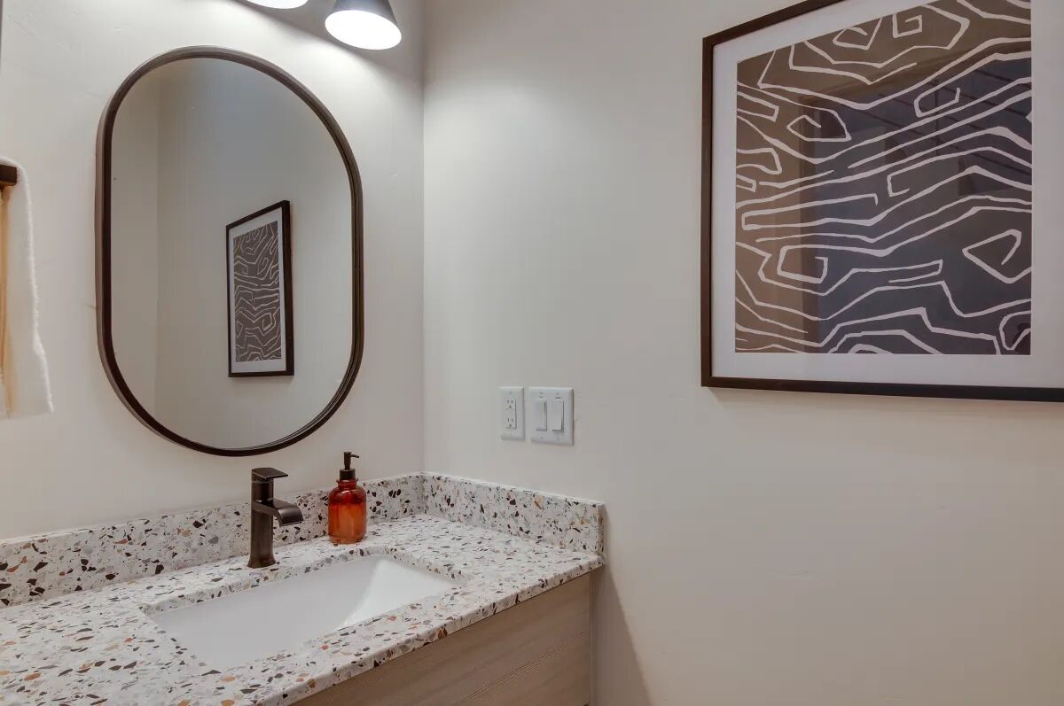 A bathroom with a white sink, a mirror, and a framed abstract artwork on the wall.